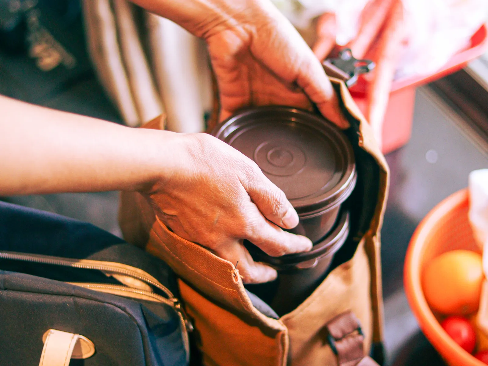 Hands sliding a stacked steel tiffin into a canvas lunch bag