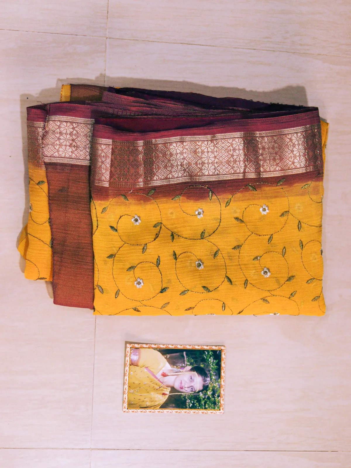 Her folded yellow and maroon wedding saree above a framed photograph of her wearing it