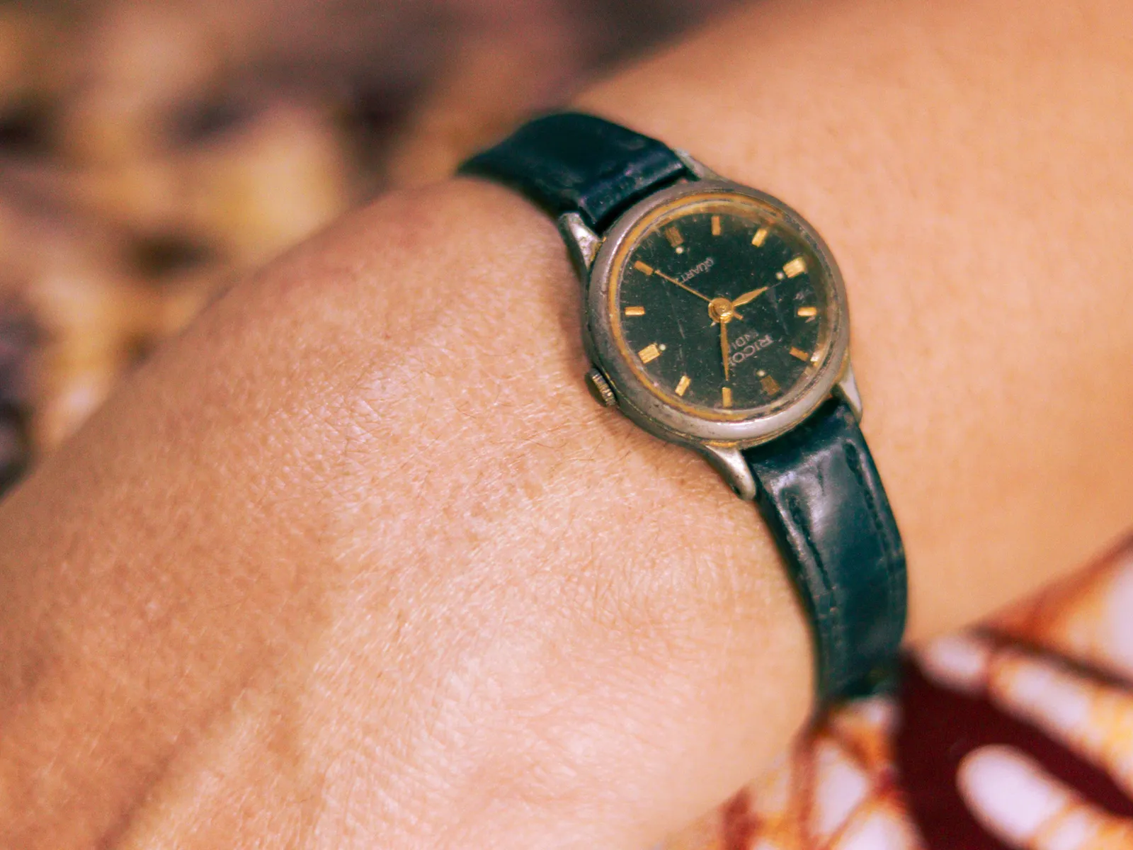Her first wristwatch, small and worn, with a black dial and cracked leather strap