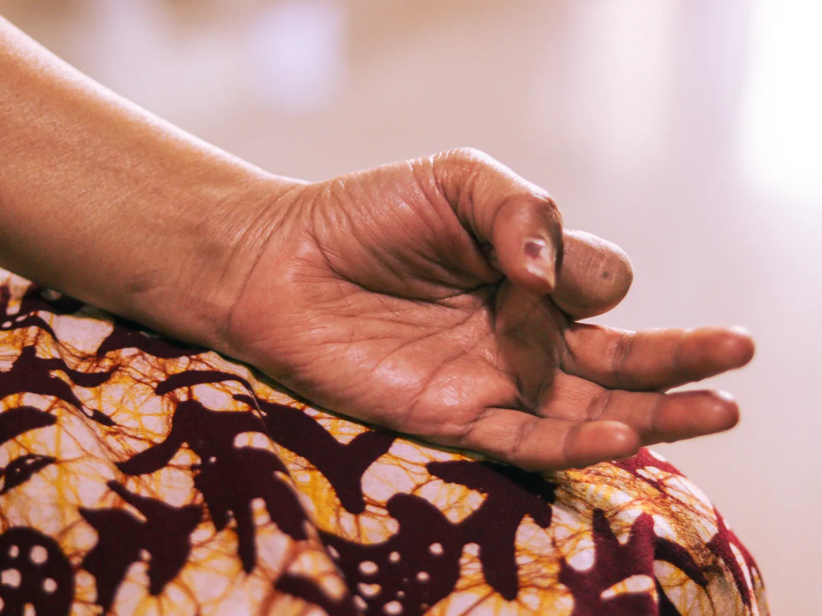 Her hand resting on her knee in a yoga mudra, thumb and forefinger touching, over a printed cotton dress